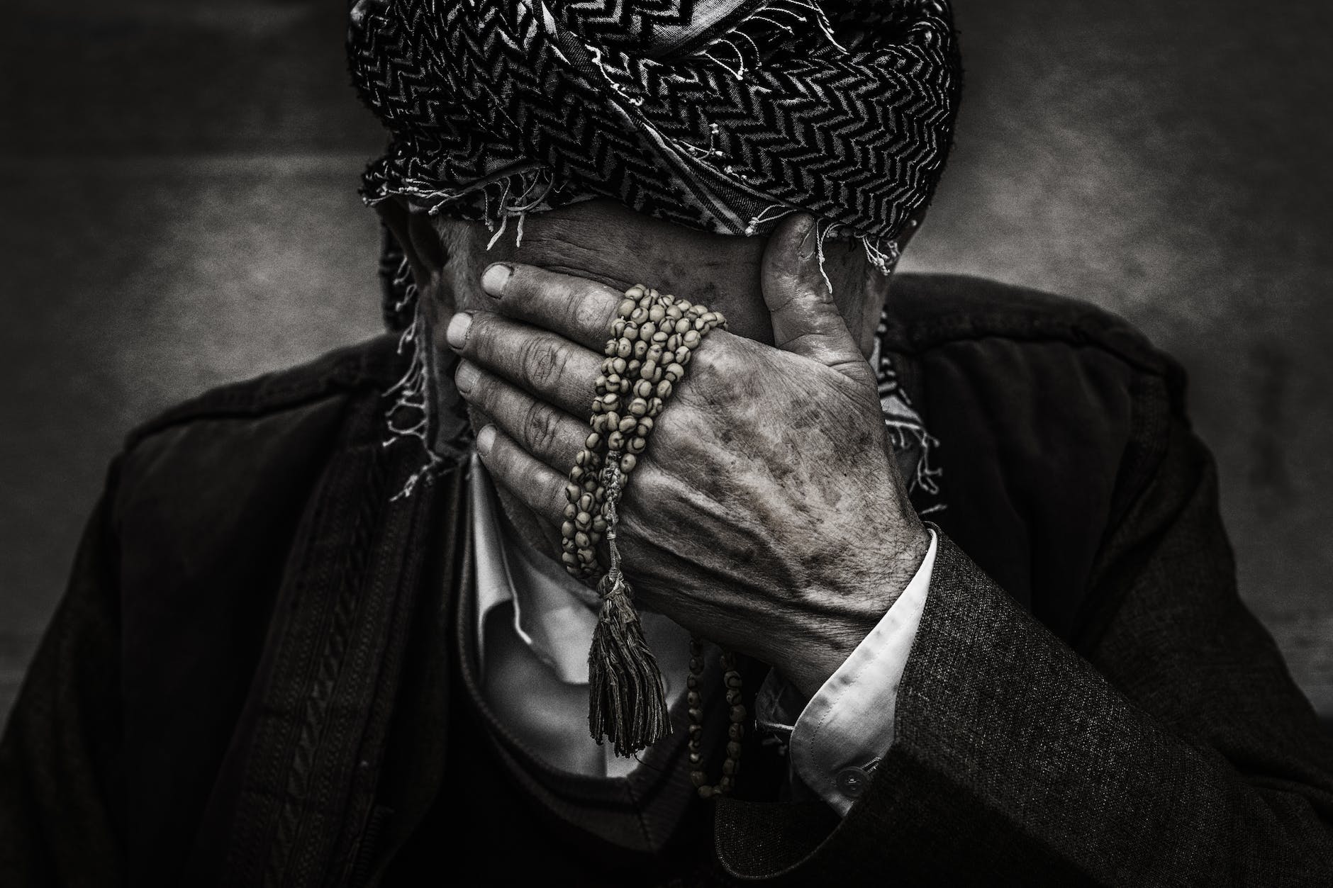 person putting palm on face while holding prayer beads