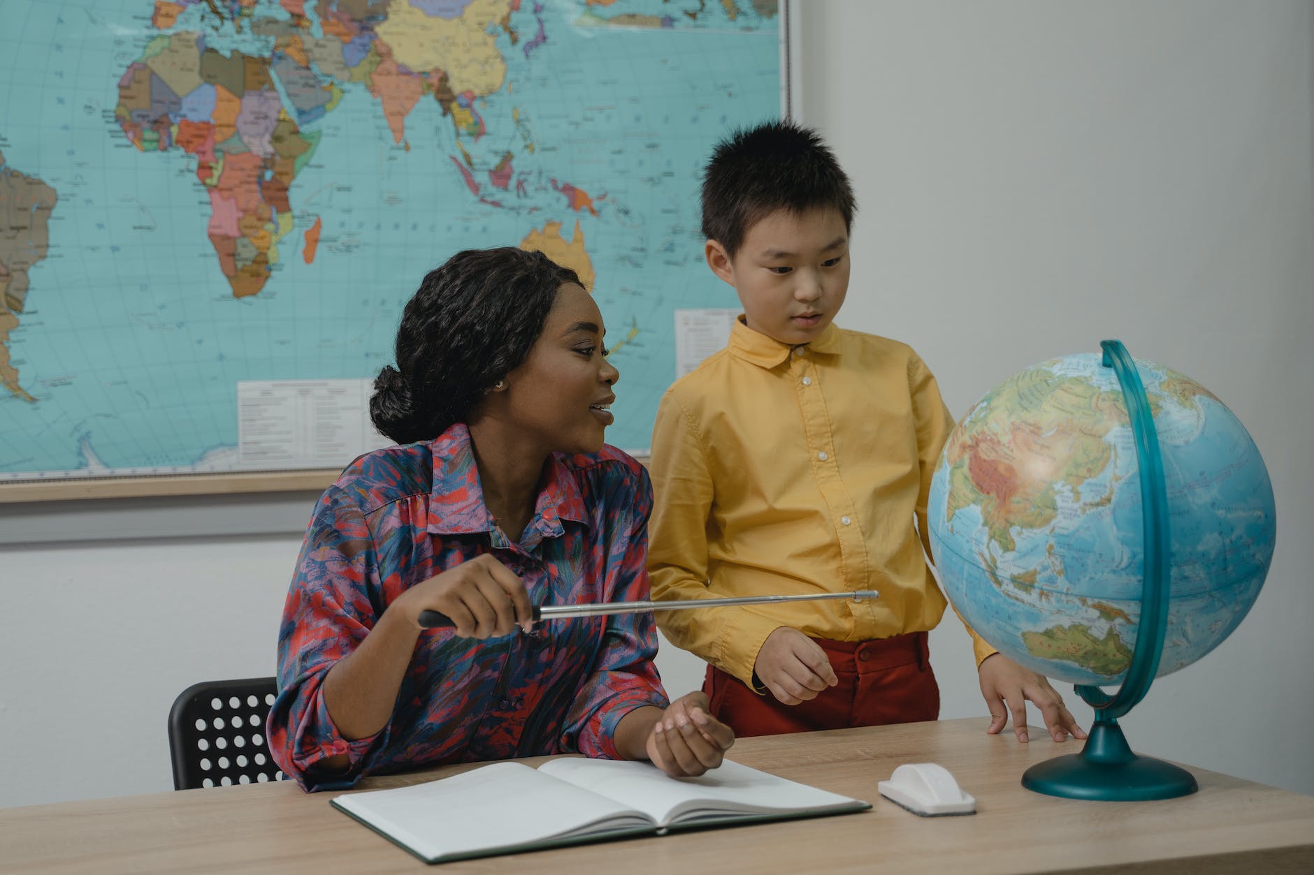 teacher pointing at a globe using a pointer